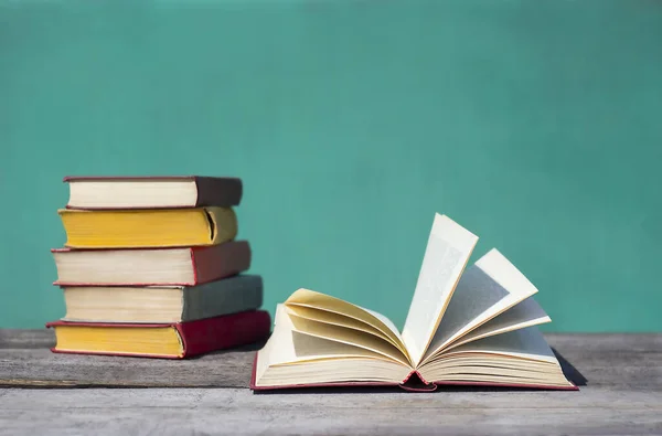 Açık bir kitap, turkuaz bir arka planda gri tahta bir masada yatıyor.