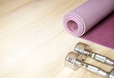 Yoga minderi ve metal dambıllar ahşap zeminde yatıyor.