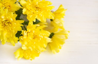 A bouquet of yellow chrysanthemums lies on a light wooden surface. Selective focus