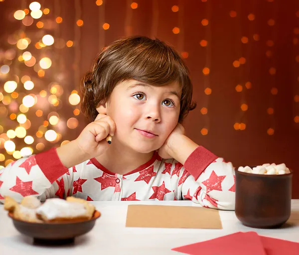 Menino Senta Uma Mesa Contra Fundo Uma Árvore Natal Escreve — Fotografia de Stock