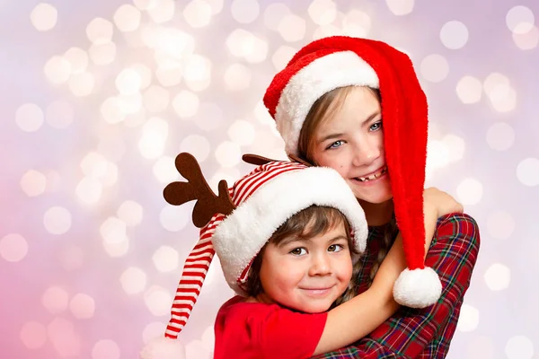 İki çocuk noel şapkası takmış, arka planda sönmüş ışıklar var.