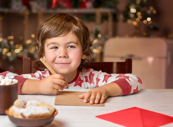 Gülümseyen çocuk mutfaktaki masaya mektup yazıyor.