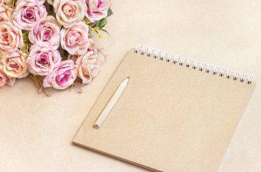 Bir kalem ve bir buket çiçekli defter kahverengi bir arka planda yatıyor.