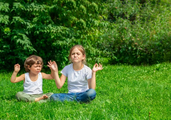 İki çocuk dışarıda çimlerde oturuyor. Parkta, Lotus pozisyonunda.