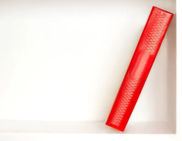 One red book stands on a white bookshelf