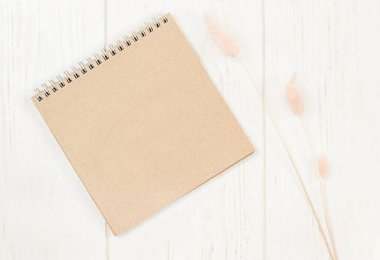 Kahverengi not defteri, kurumuş çiçeklerle dolu ahşap bir masada yatıyor.