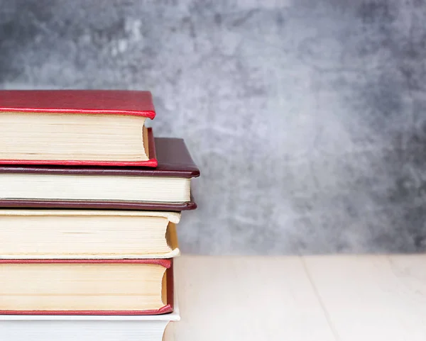 beton bir duvara karşı bir masanın üzerinde kitap yığını