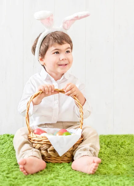 a small child in a rabbit costume sits with a basket of colored eggs