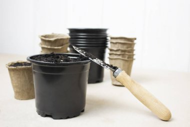 Tencere, saksı, toprak ve spatula masanın üstünde.