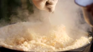 Aşçı büyük metal bir kaşıkla pirinci karıştırıyor. Bolca buhar, buharda pirinç. Lezzetli yemekler, lezzetli yemekler. Yürüyüşte açık havada yemek pişirmek. Yakın plan. Öğle yemeği için sıcak pilav. Restoran yemeği.