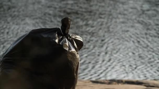 Stor svart plastpåse med skräp ligger på flodstranden. — Stockvideo