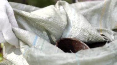 Eldivenli adam çöp torbasında eski ve paslı teneke kutuları topluyor.