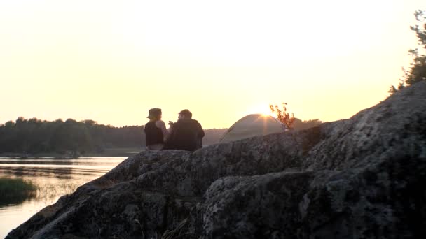 Twee mensen knuffelen, zittend op een steen in de zonsondergang stralen, achteraanzicht. — Stockvideo