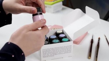 Sanatçının elleri kutudan bir kavanoz boya alır ve açar.
