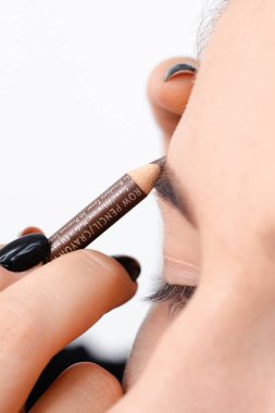 Profesyonel makyaj sanatçısı güzel bir mankene makyaj yapar. Temiz tenli bir kızın yüzü. Gerçek hayatta makyaj ve kozmetoloji konsepti. Makyöz kıza kalemle kaş çizer.