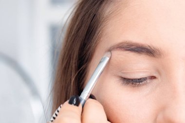 Profesyonel makyaj sanatçısı güzel kız modeline makyaj yapar. Temiz tenli bir kızın yüzü. Gerçek hayatta makyaj ve kozmetoloji konsepti. Makyaj sanatçısı fırçalı bir kıza kaş getiriyor.