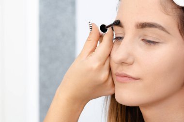 Profesyonel makyaj sanatçısı güzel kız modeline makyaj yapar. Temiz tenli bir kızın yüzü. Gerçek hayatta makyaj ve kozmetoloji konsepti. Makyaj sanatçısı müşterinin kaşlarına rimel sürüyor.