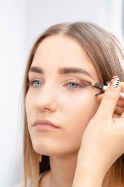 Profesyonel makyaj sanatçısı güzel kız modeline makyaj yapar. Temiz tenli bir kızın yüzü. Gerçek hayatta makyaj ve kozmetoloji konsepti. Makyaj sanatçısı makyaj stüdyosundaki göz kapaklarına gölge uygular.