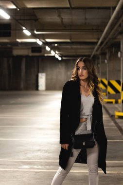 Çekici, kahverengi saçlı kadın yeraltı otoparkında poz veriyor. Siyah ceketli kız boş bir yeraltı otoparkında poz veriyor. Akşam makyajlı genç ve güzel bir kızın şık fotoğrafı.