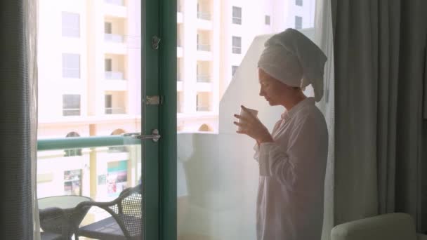 Jeune femme debout à la fenêtre au lever du soleil avec une tasse de café boisson chaude — Video