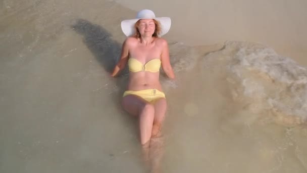 Femme en maillot de bain jaune et chapeau se trouve sur la plage à l'eau de la mer — Video