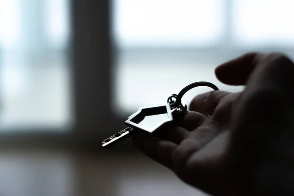 女人的手拿着钥匙和房子形状的钥匙链 靠窗的现代大堂内部 抵押贷款概念 房地产 搬家或租赁财产 — 图库照片