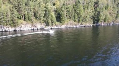 Tekne Teletskoye Gölü boyunca kayalıklar boyunca yol alır.