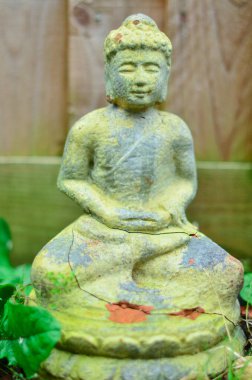 Buda 'nın küçük taş heykeli, arkasında ahşap bir çit, önü manzaralı..