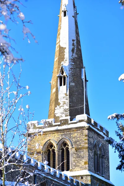 O pináculo da antiga igreja vitoriana está tudo na neve, contra o céu azul. — Fotografia de Stock