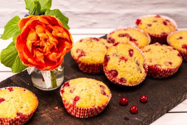 Eski ahşap bir tahtanın üzerinde bir buket çiçekle servis edilen üzümlü kekler.