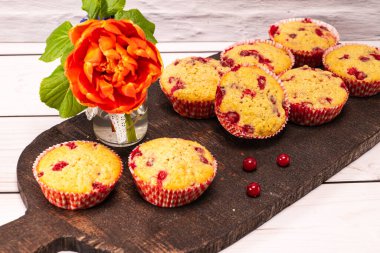 Eski ahşap bir tahtanın üzerinde bir buket çiçekle servis edilen üzümlü kekler.