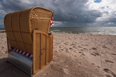 Deniz kenarındaki kumsal Alman plaj sandalyesi ve dramatik gök gürültüsü bulutlarıyla