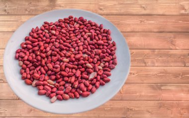 Sağlıklı beslenmek için eski ahşap masa arkaplanındaki tabakta duran kuru kırmızı kabuklu çiğ fıstık manzarası. Vejetaryen ve vejetaryen yemekleri. Kırsal biçim.