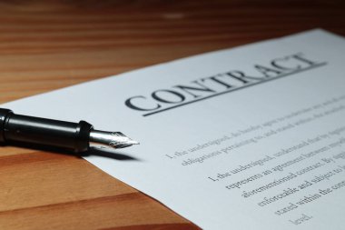 Fountain pen lain across contract paperwork against wooden table top 
