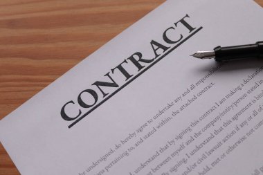 Fountain pen lain across contract paperwork against wooden table top 