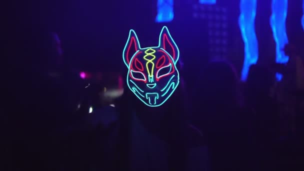 Kobieta tańcząca w neonowej masce w środku tłumu tańczących ludzi na koncercie w nocnym klubie. — Wideo stockowe
