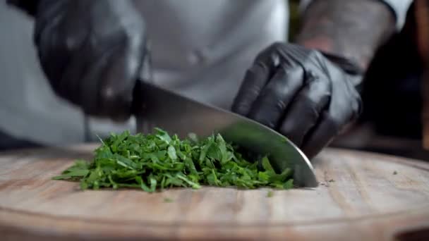 Шеф-повар в черных перчатках отбивает петрушку на деревянной доске — стоковое видео