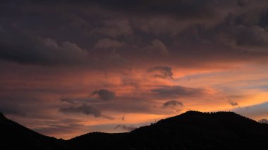 Karanlık tepelerin üzerinde yumuşak renkli günbatımı bulutları