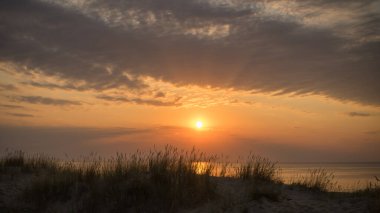Jurmala Letonya 'da çimlerle kaplı bir plajın üzerinde ılık bulutlu gün batımı ışığı