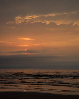 Gün batımından önce bulutlara batan beyaz bir güneş sakin Baltık Denizi üzerinde