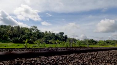 Çakıl taşlarını yastık olarak kullanan tren rayları, yeşil pirinç tarlalarını geçen, gündüz mavi gökyüzü arka planı