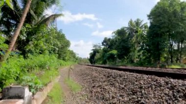 Çakıl taşlarını yastık olarak kullanan tren rayları, yeşil pirinç tarlalarını geçen, gündüz mavi gökyüzü arka planı