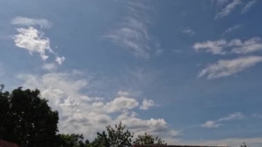 Açık mavi gökyüzü, beyaz bulutlar, tropik iklimde sıcak hava, bol güneş ışığı ve yeşil yapraklar.