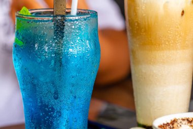 Köpükler ve çiy damlaları soğuk içecek bardağına yapışmış, ferahlatıcı mavi bitkisel içecek.