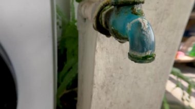 The water faucet made of blue plastic looks dirty, overgrown with moss, it doesn't work properly, there are clean water droplets in slow motion