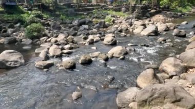 Surface of a small river near a volcanic mountain, rocks from volcanic activity scattered along the river, a river that is the path of the cold lava of Mount Merapi in Java