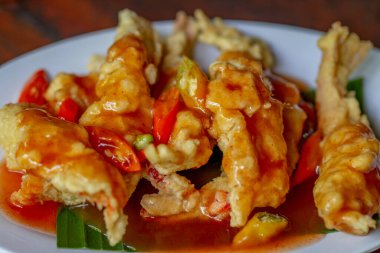 Deep-fried prawns topped with sweet and sour sauce served on a white plate lined with banana leaves, fresh seafood preparations for lunch