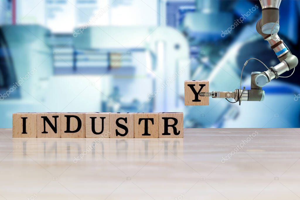 Industrial robot picking wooden letter for build message on wooden desk and machine blue tone color on blurred background, informative and communication about industry 4.0 concept