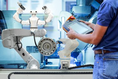 Endüstriyel robotikleri kontrol etmek için kablosuz uzaktan kumandayı kullanan yakın çekim teknisyeni akıllı fabrika mavi ton arka planı, endüstri 4.0 konsepti üzerinden otomasyon üretiminde çalışıyor.