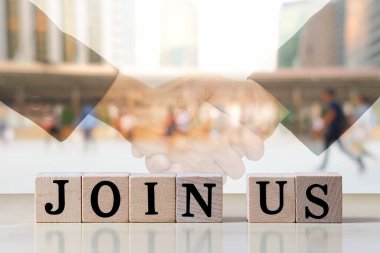 Tahta küp mektup, ahşap masada bize katılması için mesaj oluşturur. Çift taraflı iş tokalaşması ve şehir arka planındaki bulanık insanlar, iş konsepti, kopyalama alanı.